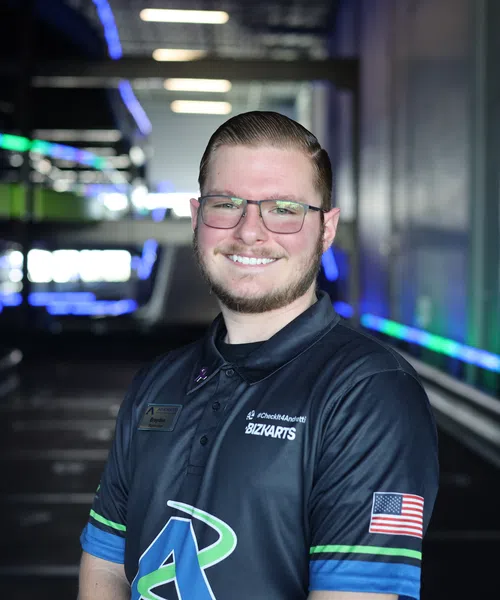 Smiling man in black Bizzarts shirt with American flag patch in neon-lit parking garage.