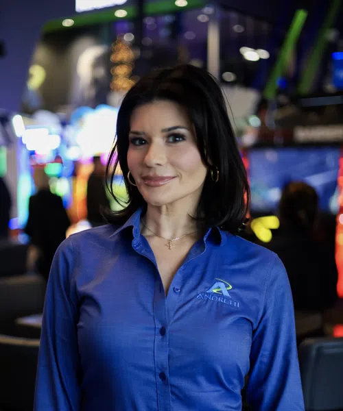 Smiling woman in blue shirt with Amoretti logo stands in a colorful, blurred indoor setting.