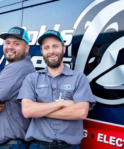 Two smiling HVAC technicians in uniform stand confidently in front of a Badger Boilers Services van.