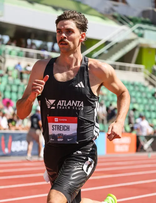 Male athlete running on track in black Atlanta Track Club uniform during daytime competition