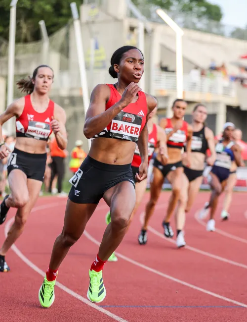 Female athlete Baker sprinting on an outdoor track during a competitive race with other runners behind her.