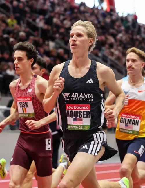 Male athletes competing in an indoor track race with a crowded stadium in the background