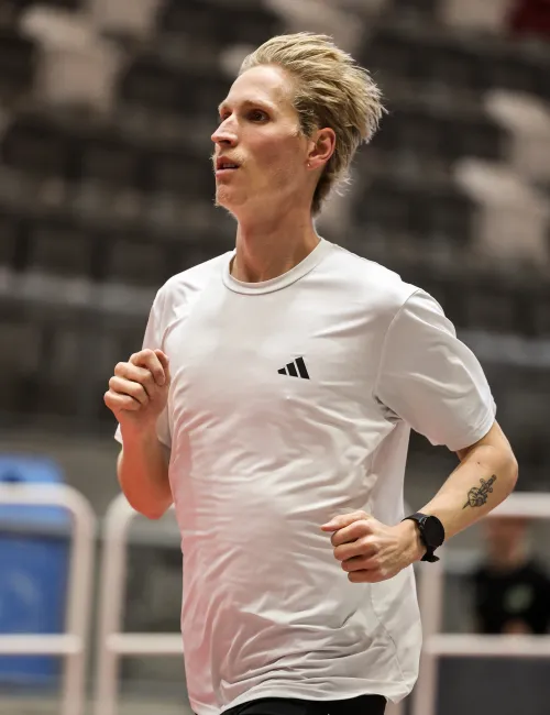Young man running indoors wearing white adidas shirt and black shorts with tattoo and sports watch