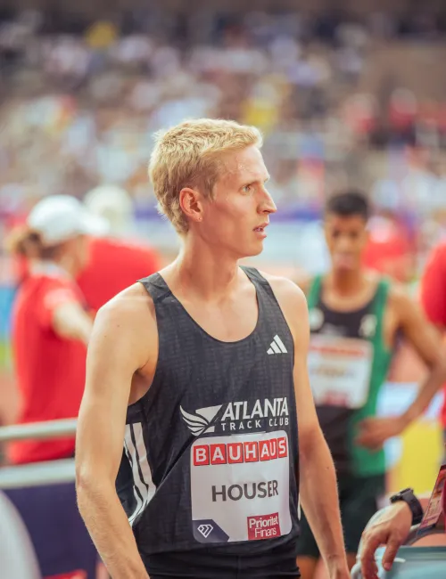 Blond male athlete in black Atlanta Track Club singlet at a competitive track event, focused and ready.