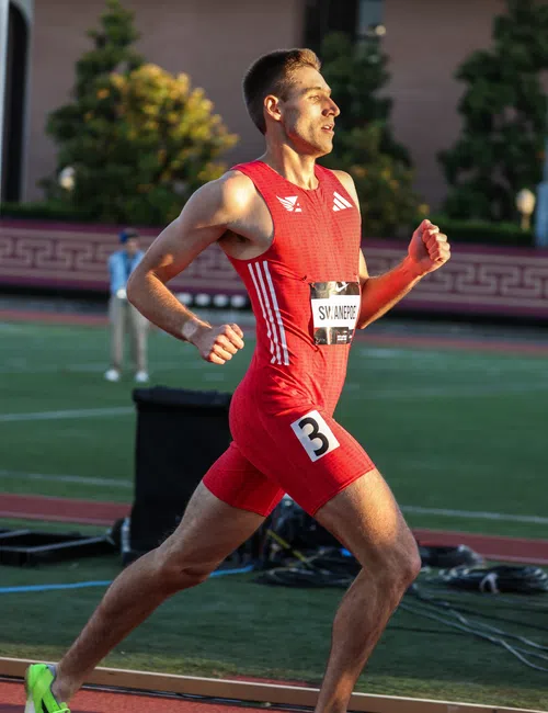 Male athlete in red running gear sprinting on track with neon green shoes during outdoor race.