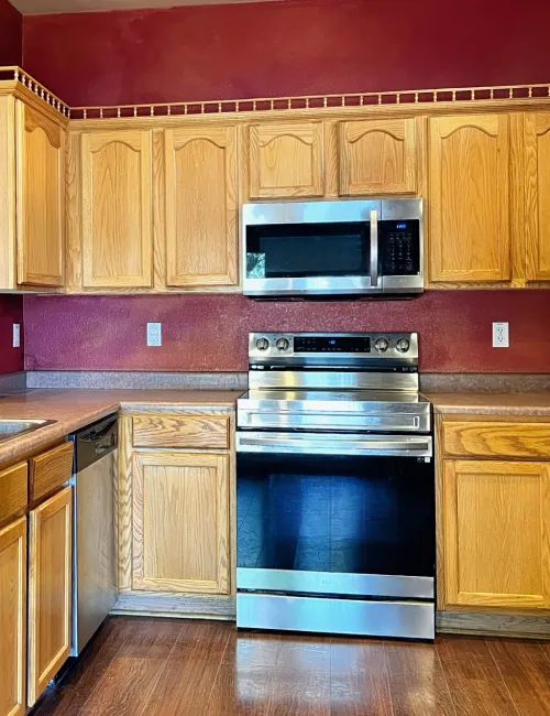 Modern kitchen with oak cabinets, stainless steel appliances, double sink, and bold red walls