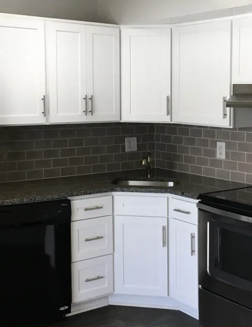 Modern kitchen with white cabinets, stainless steel appliances, granite countertops, and gray subway tile backsplash.