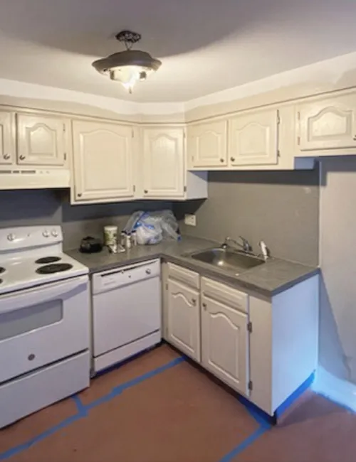 Small kitchen with white cabinets, electric stove, dishwasher, single sink, gray countertops, and overhead light fixture.