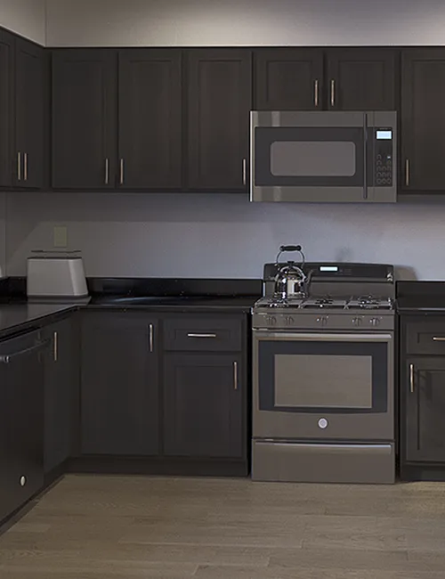 Modern kitchen with dark wood cabinets, stainless steel appliances, and light hardwood flooring in an L-shaped layout.