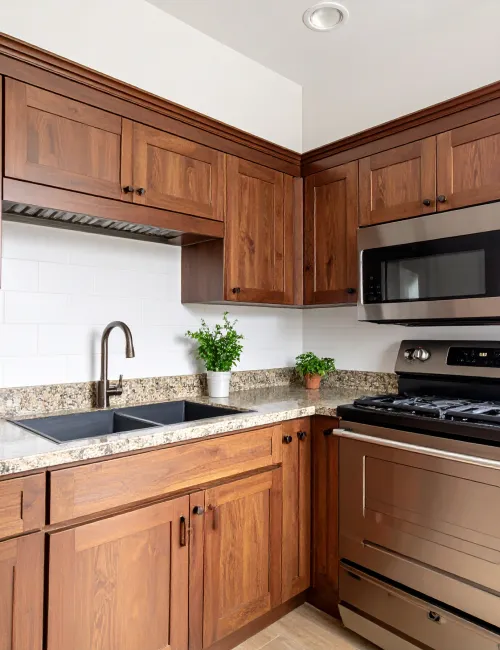 Modern kitchen with wooden cabinets, granite countertops, stainless steel stove, microwave, and black sink with plants.