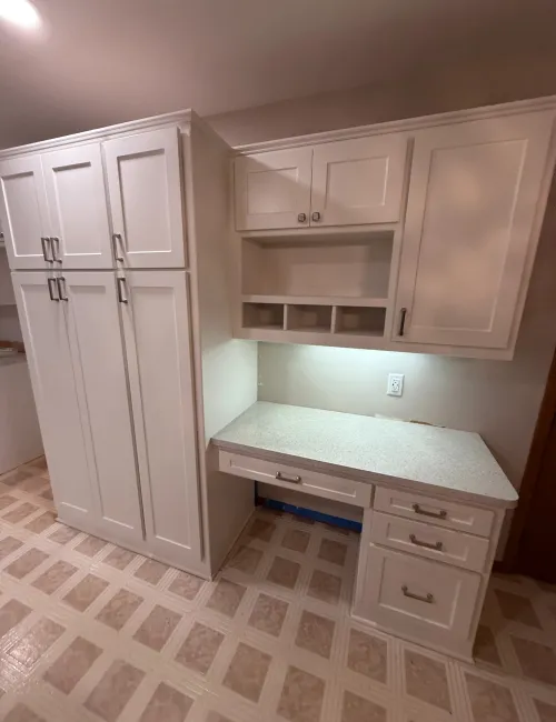 White kitchen cabinets with drawers and shelves against a patterned tile floor in a neutral-toned room.