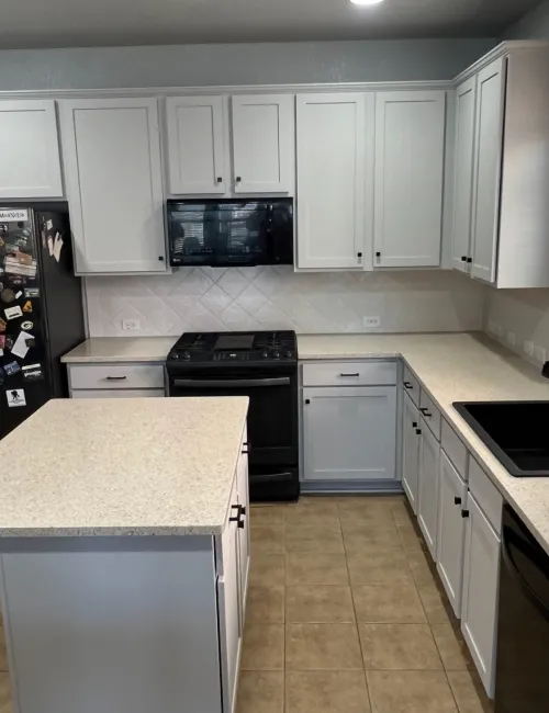 Modern kitchen with white cabinets, black appliances, tiled floor, and granite countertops under natural light.
