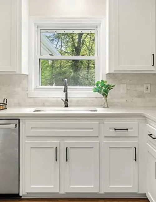 Modern white kitchen with stainless steel appliances, black handles, subway tile backsplash, and a window above the sink.