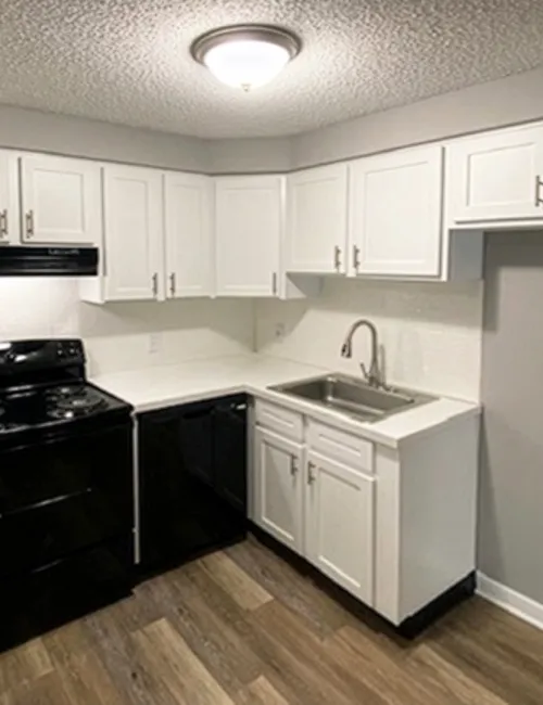 Modern white kitchen with black appliances, wood flooring, and overhead lighting in a compact layout