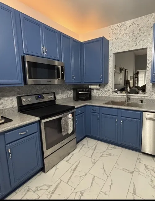 Modern kitchen with blue cabinets, stainless steel appliances, gray countertops, and marble tile flooring.