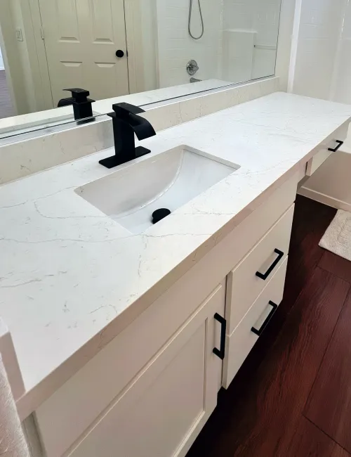 Modern bathroom vanity with white marble countertop, integrated sink, matte black faucet, and wooden floor.
