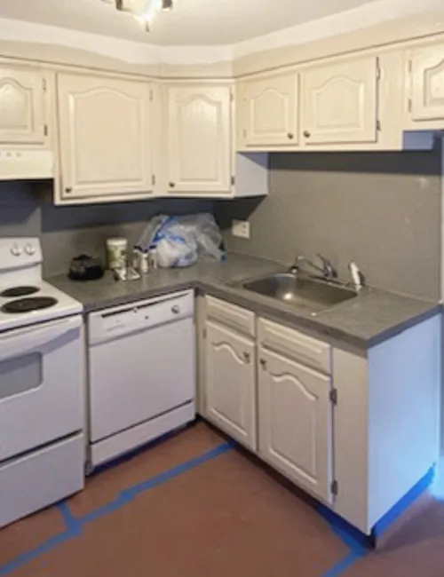 Compact kitchen with white cabinets, electric stove, dishwasher, and single sink under soft lighting.