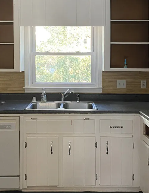 Bright kitchen with white cabinets, black countertops, open shelves, double sink under window, and dishwasher.