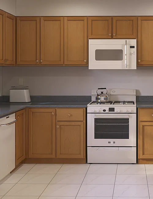 Modern kitchen with wooden cabinets, white appliances, gray countertops, and tiled white floor under bright lighting