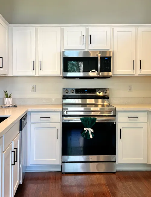 Modern white kitchen with stainless steel appliances, hardwood floors, black faucet, and marble countertops.