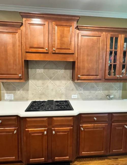 Kitchen with wooden cabinets, white countertop, built-in gas stove, and beige tiled backsplash.
