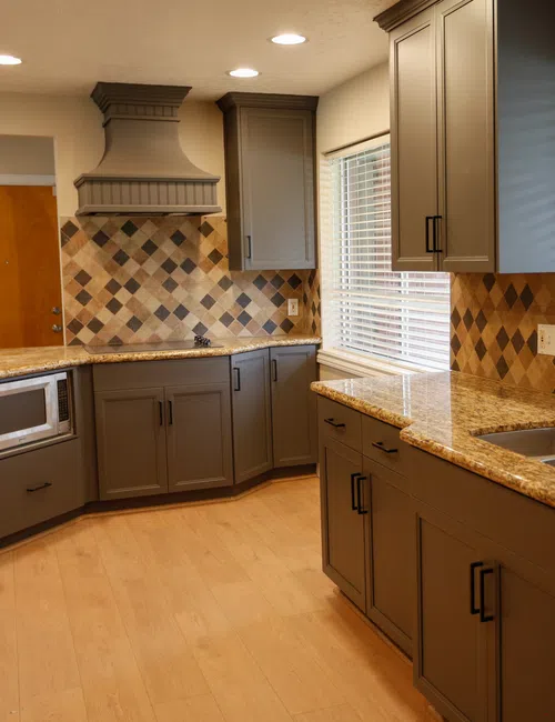 Modern kitchen with granite countertops, gray cabinets, tiled backsplash, stainless steel sink, and natural light from windows.