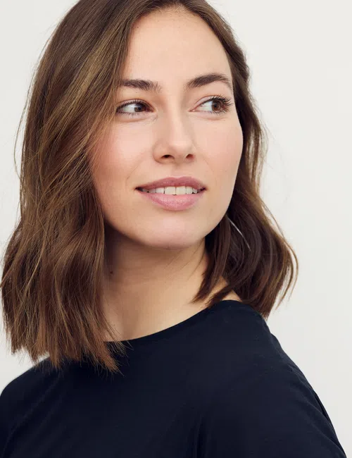 Young woman with shoulder-length brown hair wearing a black shirt looking to the side against a white background