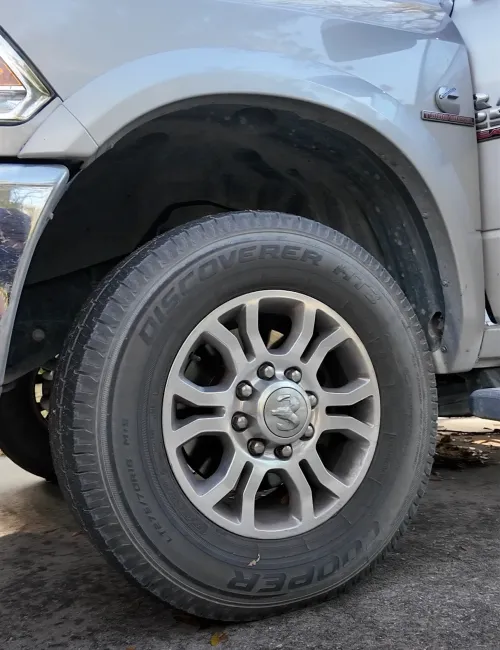 Close-up of a silver Dodge truck wheel with Cooper Discoverer AT3 tire on asphalt ground.