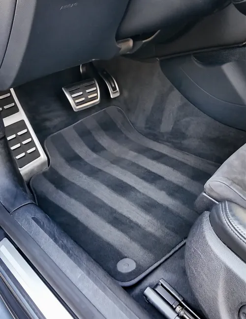 Clean black car floor mat with silver metal pedals and dark interior upholstery inside vehicle.