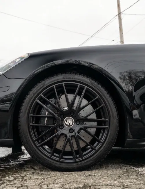 Close-up of a black sports car wheel with multi-spoke rim and brake disc on wet pavement.