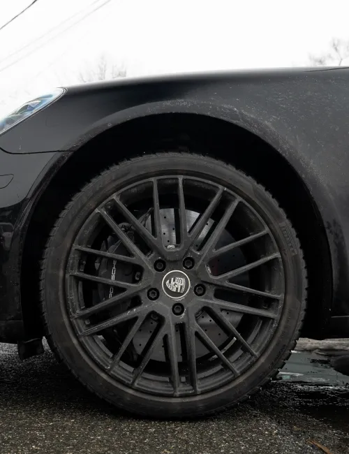 Close-up of a black sports car front wheel and tire with detailed alloy rim on wet pavement with some snow.