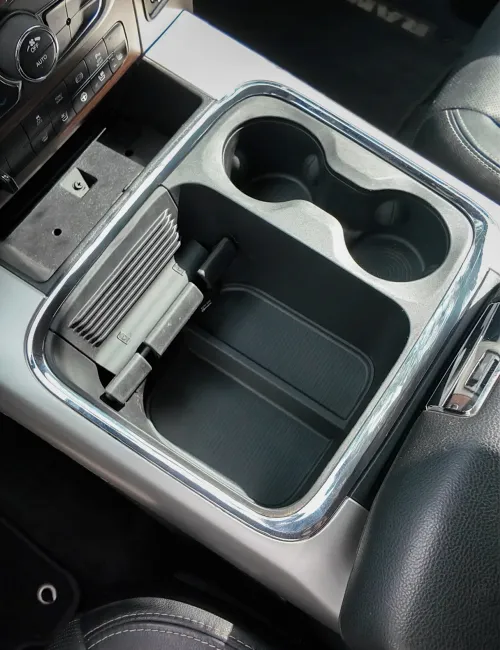 Close-up of a vehicle's central console cup holders and storage compartment with chrome trim and black interior.