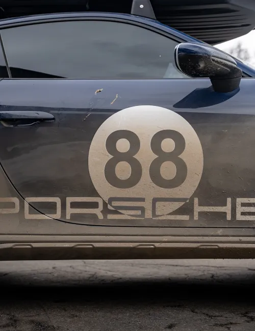 Side view of a dirty Porsche race car with number 88 decal on the door and spoiler attached at the back.