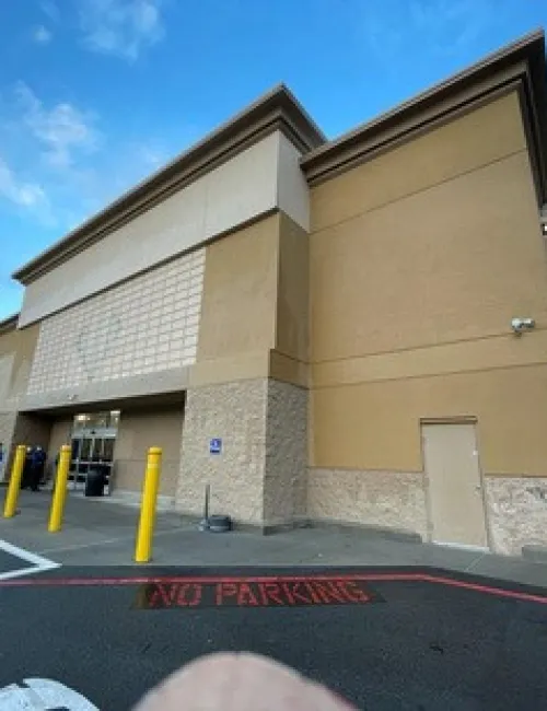 Exterior of a beige commercial building with yellow bollards, 'No Parking' zone, and a clear blue sky.