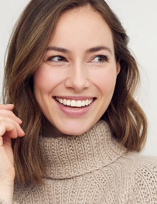Smiling woman wearing a cozy beige knit turtleneck sweater looking to the side against a plain background