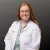 Smiling female healthcare professional with red hair wearing glasses and a white lab coat against a dark background