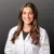 Smiling female scientist with long brown hair wearing a white lab coat against a dark gray background