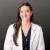 Young female doctor with long brown hair wearing a white lab coat and navy scrubs against dark background