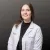 Smiling female doctor in white lab coat against gray background, professional healthcare portrait.
