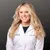 Smiling female doctor with long blonde hair wearing a white lab coat, standing against a dark background.