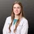 Professional portrait of a female healthcare provider wearing a white lab coat against dark background.