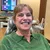 Smiling woman in green sweater sitting in a dental office chair with dental tools and computer screen in the background
