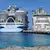 Two large cruise ships docked side by side at a pier with clear blue water and sky.