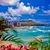 Waikiki Beach with turquoise water, surfers, city skyline, Diamond Head crater, and tropical foliage under a blue sky.