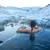 Person relaxing in a hot spring surrounded by snow-covered rocky landscape under clear sky