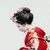 Traditional Japanese geisha in a red floral kimono with elaborate hair ornaments bowing gracefully.