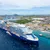 Large Celebrity Beyond cruise ship docked near tropical coastline with clear blue waters and city landscape in background