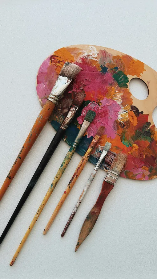 Artist’s paint palette covered in mixed colorful oil paints with six used paintbrushes laid out beside it.