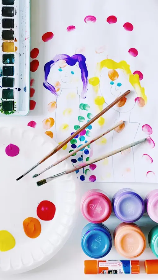 Watercolor paints, brushes, and paper with colorful dot artwork in a creative painting setup.