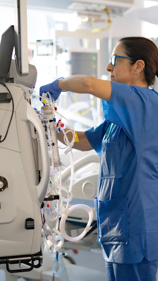 Medical professional in scrubs adjusting equipment in a hospital room.